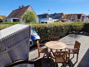 Ein Sitzbereich im Freien mit einem runden Tisch und Holzstühlen, umgeben von einer Hecke und einem Kiesweg.