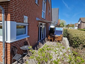 Ein Backsteinhaus mit einer Terrasse, die einen Tisch und Stühle, eine überdachte Sitzgelegenheit und einen Heckenabschnitt bietet.