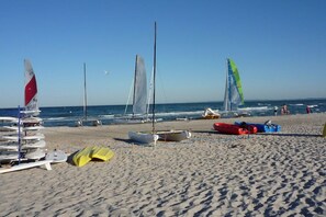 A beach with sailboats and kayaks, a clear sky, and the ocean in the background. - Penthouse Swallow's Nest (Damp)