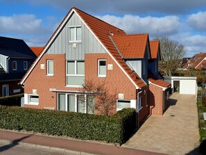 Ein zweistöckiges Wohngebäude mit rotem Ziegeldach, Backsteinfassade und einem kleinen Vorgarten mit Hecke.