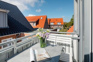 Ein Balkon mit weißer Brüstung, einer Blumenvase und einer Zeitschrift auf dem Boden.