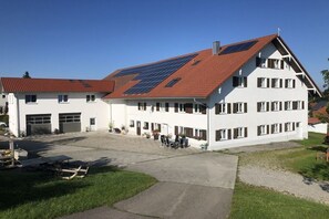 A two-story building with a red-tiled roof, solar panels, and a covered outdoor seating area. - Ferienhof Schönmetzler “Hofblick” (Altusried\/ Muthmannshofen)