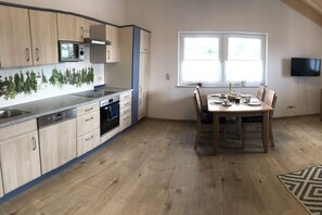 A compact kitchen with a dining area, wooden cabinets, a microwave, and a television. - Ferienhof Schönmetzler “Hofblick” (Altusried\/ Muthmannshofen)