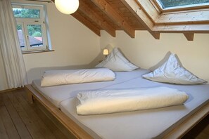 Ein Schlafzimmer mit Holzbalkendecke, einem Oberlicht, einem Bett mit weißer Bettwäsche und einem Fenster mit Vorhängen.