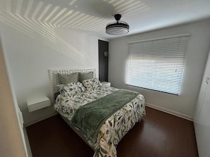 Ett sovrum med en säng, en takfläkt, ett fönster med persienner och en väggmonterad lampa.