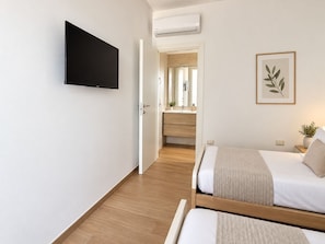 A hotel room with a TV mounted on the wall, a bed with a headboard, a bedside table with a lamp, and a framed plant on the wall. - Ponente Privé Pool & Garden Retreat Salento (Lequile)