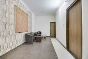 A hallway with patterned wall tiles, a seating area with leather chairs and ottomans, a glass-top table, and a wooden door with a number.