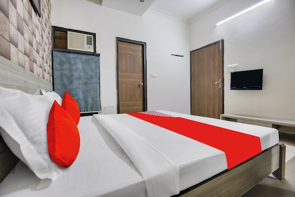 A hotel room with a bed, a television on the wall, and a window with blinds.