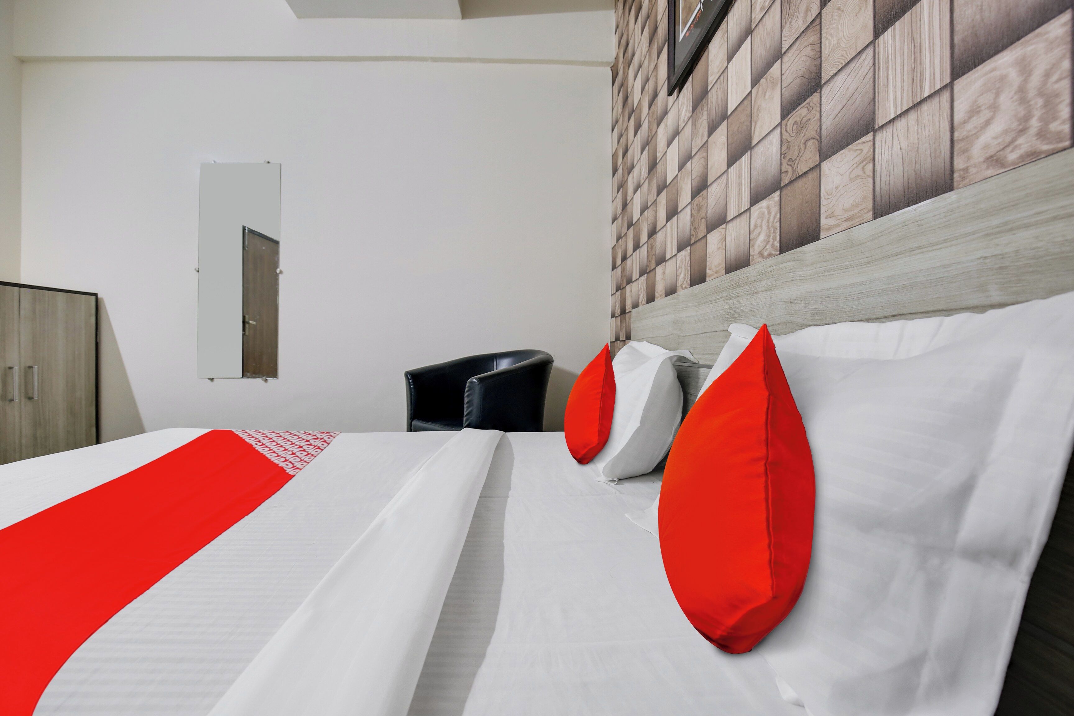 A hotel room with a bed, a wardrobe, a mirror, and a wall with a patterned design.
