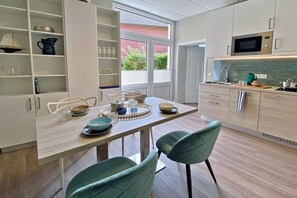 A modern kitchen with white cabinetry, a dining table set with plates and glasses, and a view of the outdoors through a window. - 2 - House Windröschen (Borkum)