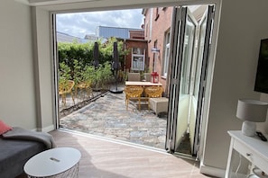 A modern room with a sliding glass door leading to an outdoor patio area with a table and chairs, a sofa, and a small round table. - 2 - House Windröschen (Borkum)