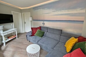 Olohuoneessa on harmaa sohva, litteänäyttöinen televisio, valkoinen sivupöytä ja pyöreä sohvapöytä.