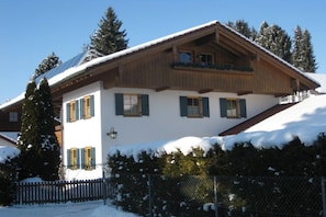 A two-story chalet with a sloped roof, wooden exterior, and a snow-covered ground. - Ellen Raith - Apartment 2 (Füssen)