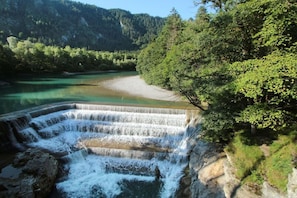 A multi-tiered waterfall structure with a river flowing through it, surrounded by dense forest and hills in the background. - Ellen Raith - Apartment 2 (Füssen)