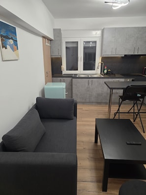 A modern kitchen with grey cabinets, a dining area with a black table and chairs, and a grey sofa. - Modern apartment in Thessaloniki (Θεσσαλονίκη)