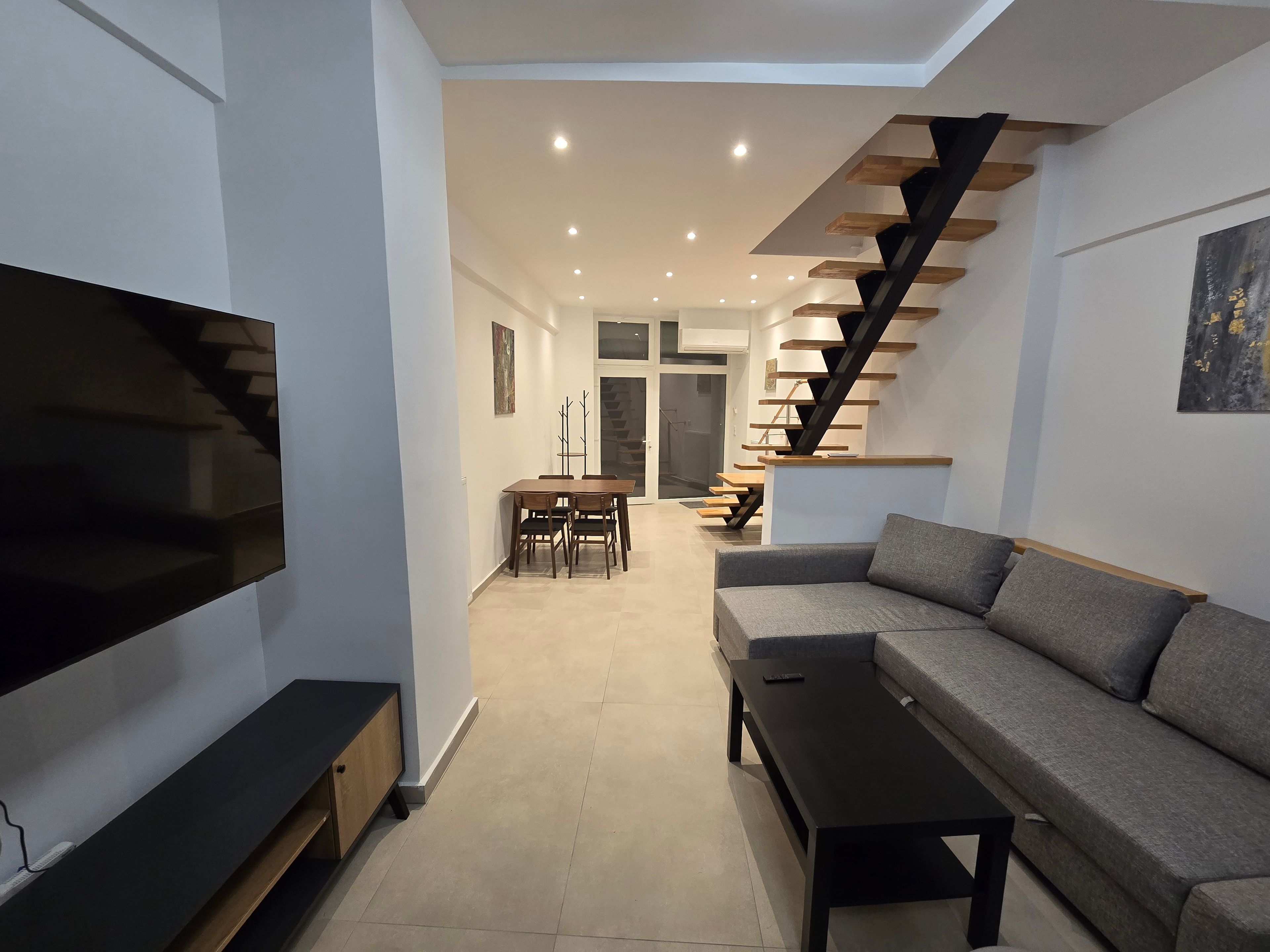 Ein modernes Wohnzimmer mit einem Flachbildfernseher, einer Couch, einem Couchtisch und einer Treppe mit Holzstufen.