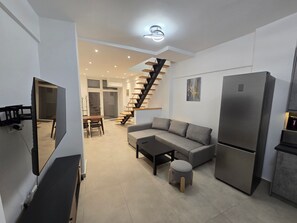 A modern living space with a sofa, coffee table, and a small stool. A staircase with wooden steps leads to an upper level. - Holiday Home 'Modern Apartment' with Wi-Fi and Air Conditioning (Θεσσαλονίκη)
