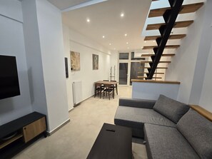 A modern living room with a grey sofa, a coffee table, a TV on a stand, a dining area with a table and chairs, and a staircase with wooden steps. - Holiday Home 'Modern Apartment' with Wi-Fi and Air Conditioning (Θεσσαλονίκη)