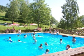 A swimming pool with people in the water, surrounded by a fence and trees. - Country House Jäger Holiday Apartment No. 1 (Todtnauberg)