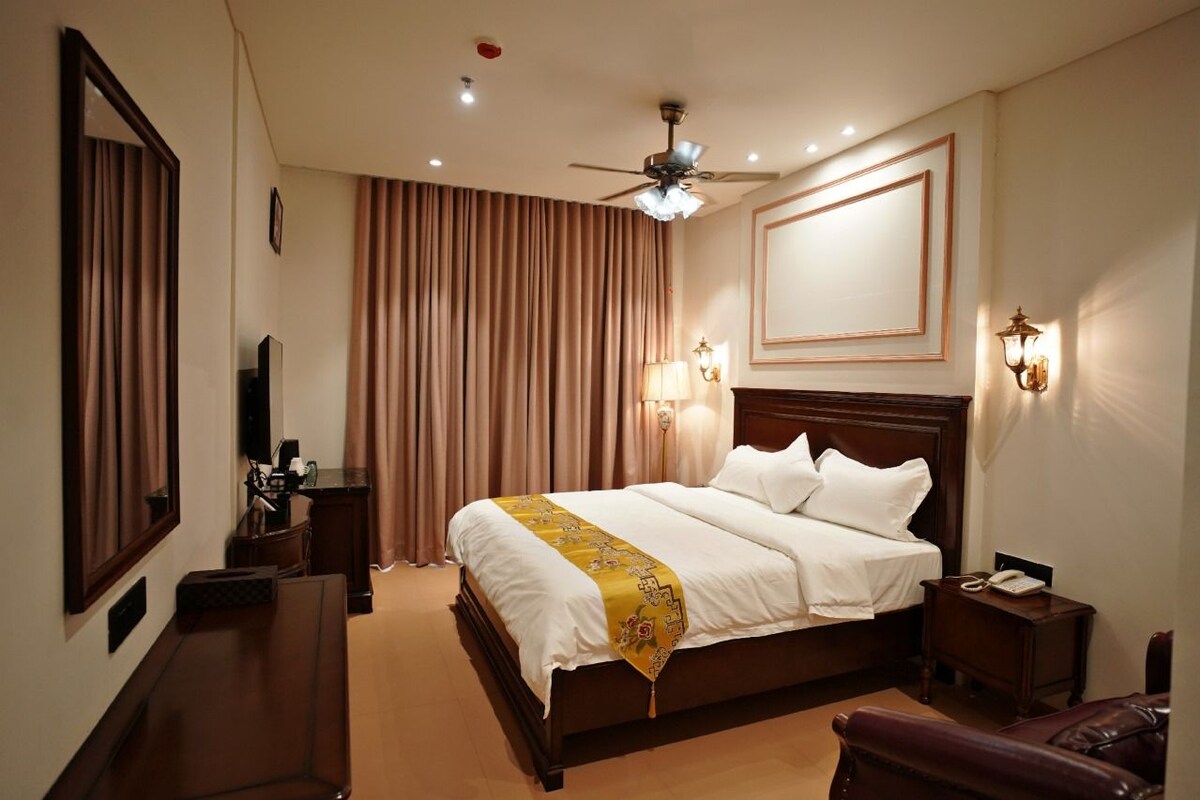 Una habitación de hotel con cama, mesita de noche, lámpara y ventilador de techo.