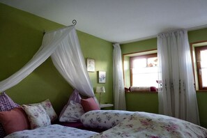 A room with a bed, a nightstand, a window with curtains, and a wall with a picture. - Holiday apartment with 2 bedrooms (Görisried)