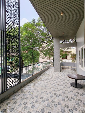 A covered outdoor area with patterned floor tiles, a metal railing, and a view of trees and buildings. - SAKET VILLA (Varanasi)