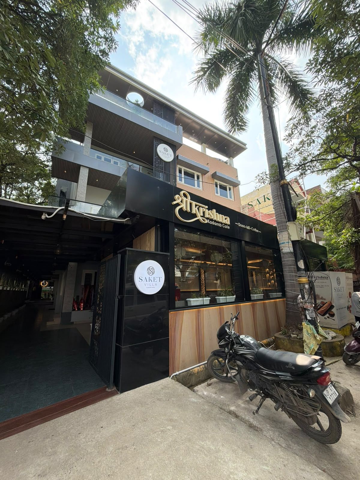 A building with a sign for 'Krishna Kadamb Cafe' and a parked motorcycle.