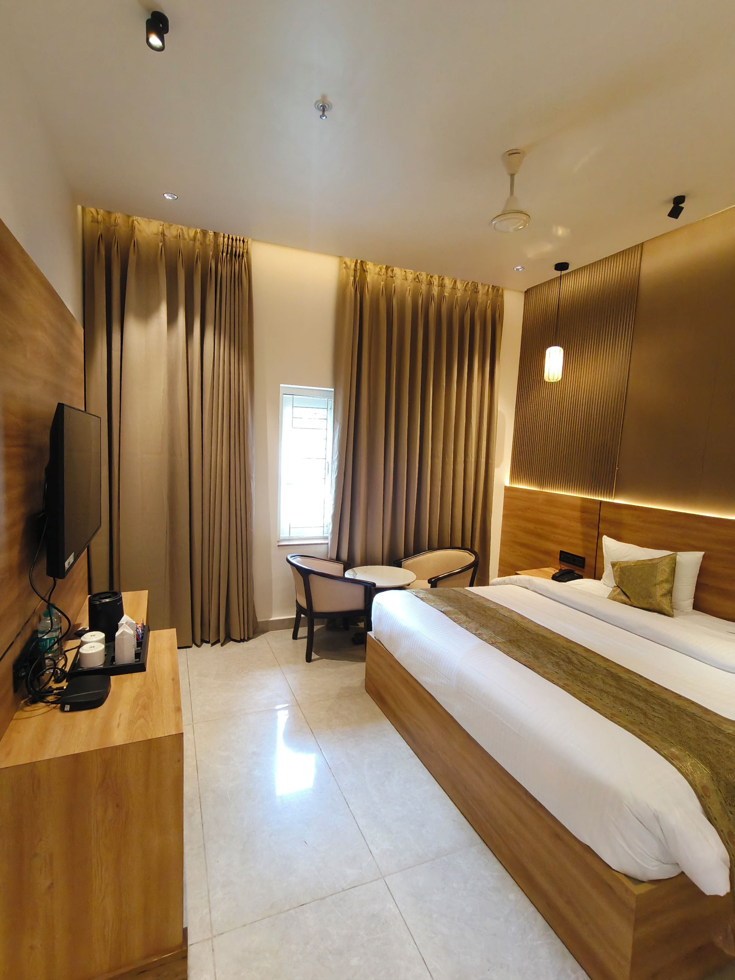 A hotel room with a bed, a desk with a television, a chair, and a small table.