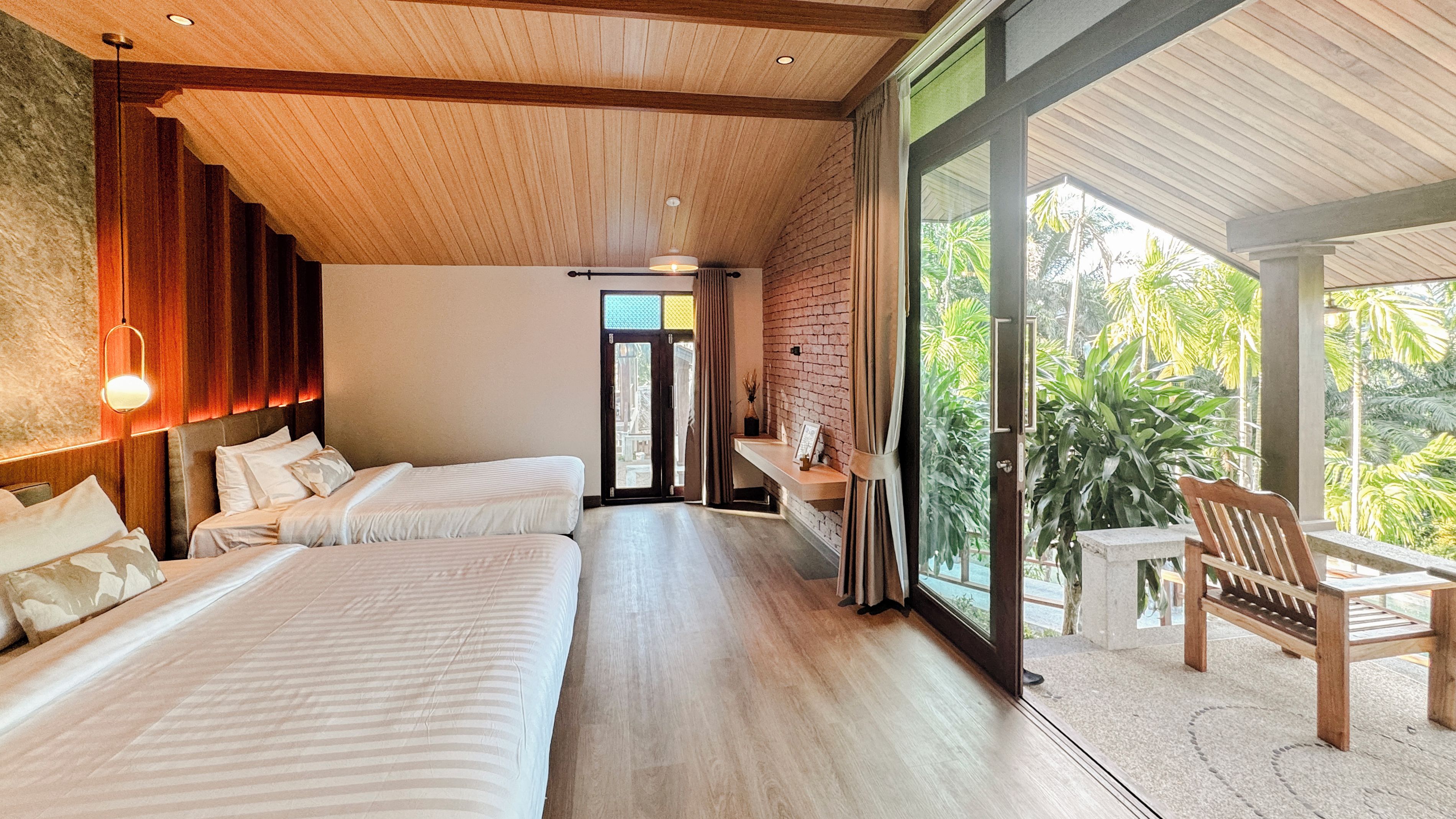A hotel room with two beds, a wooden ceiling, a large window, and a balcony with a chair.