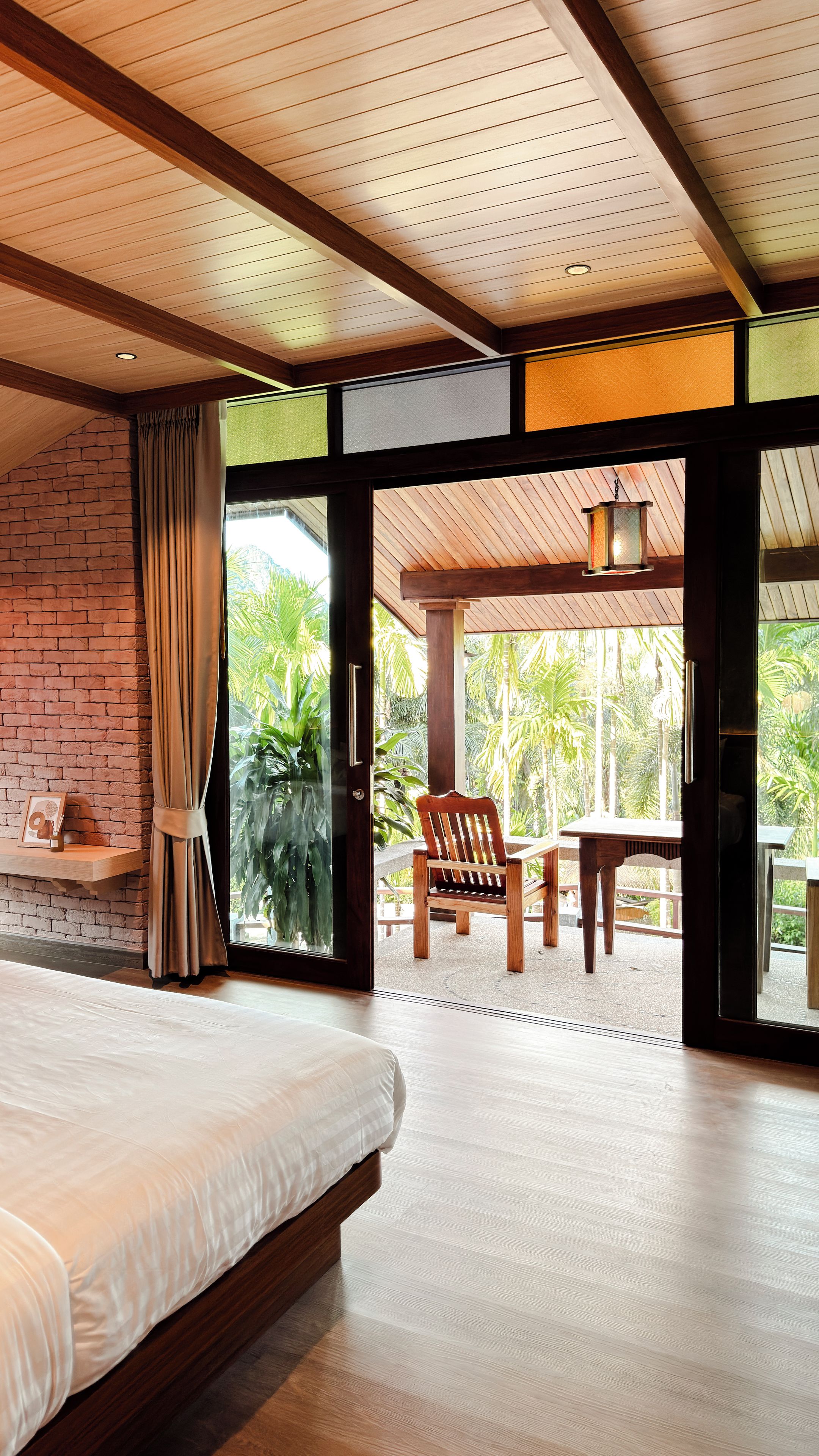 A bedroom with a large bed, a wooden ceiling, and a view of a patio with a chair and table.