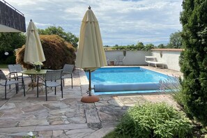 A swimming pool with a stone patio, two umbrellas, and outdoor furniture. - Holiday apartment in Salem with swimming pool (Salem)