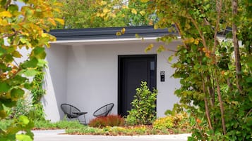 A modern building with a black door, two black chairs, and a garden with various plants.