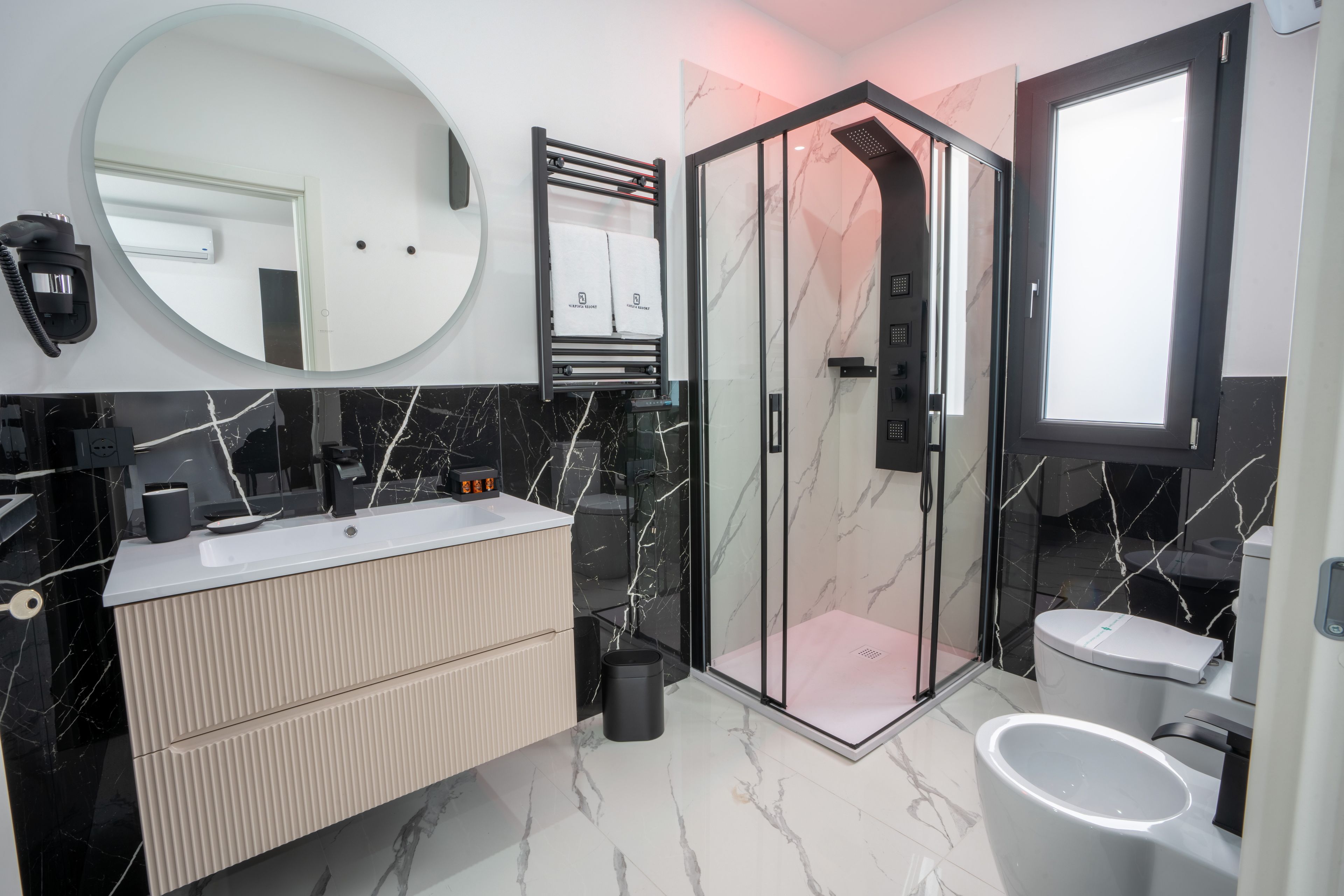 Ein modernes Badezimmer mit einer gläsernen Duschkabine, einem großen Spiegel und einem Waschtisch.