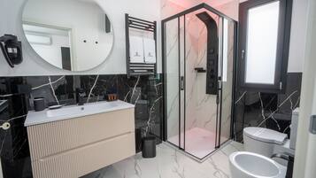 Ein modernes Badezimmer mit einer gläsernen Duschkabine, einem großen Spiegel und einem Waschtisch.