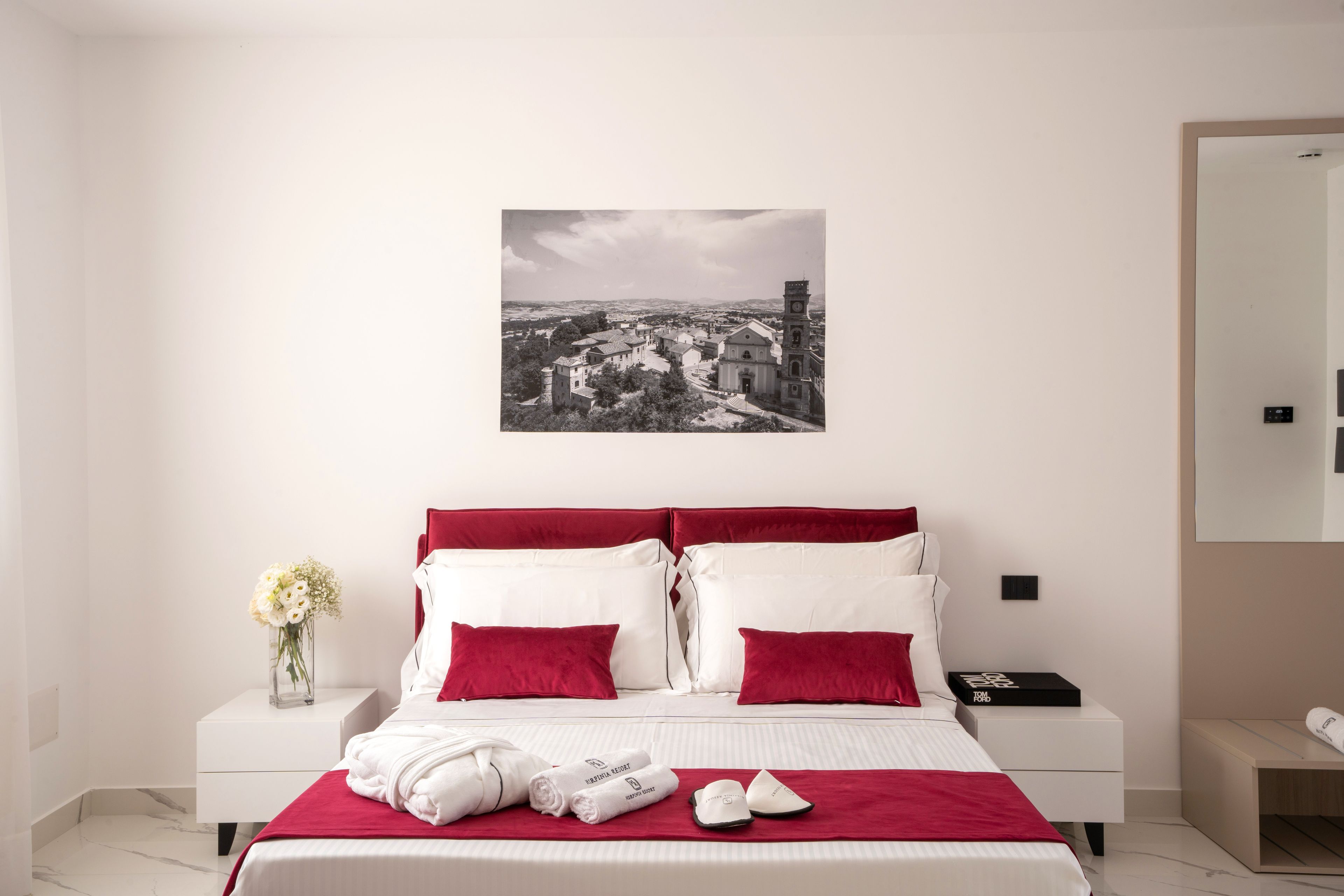 Una habitación de hotel con cama, mesita de noche, un jarrón con flores e imagen enmarcada en la pared.