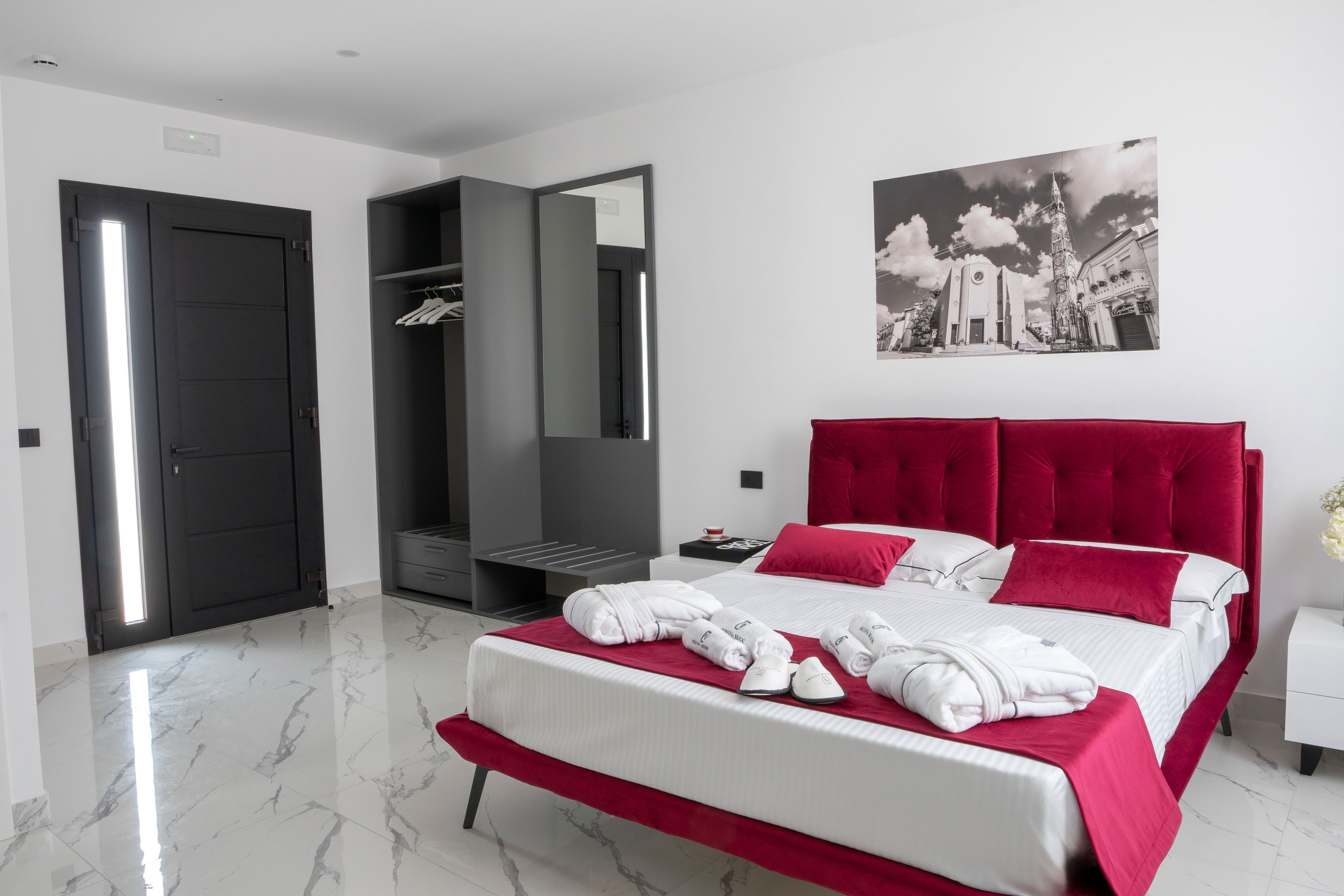 A modern bedroom with a large bed, a wardrobe, a mirror, and a wall-mounted picture.