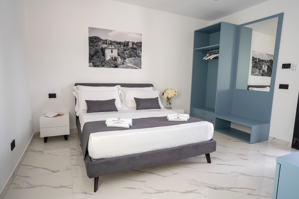 Een moderne slaapkamer met een bed, een nachtkastje, een spiegel en een aan de muur bevestigd schilderij.