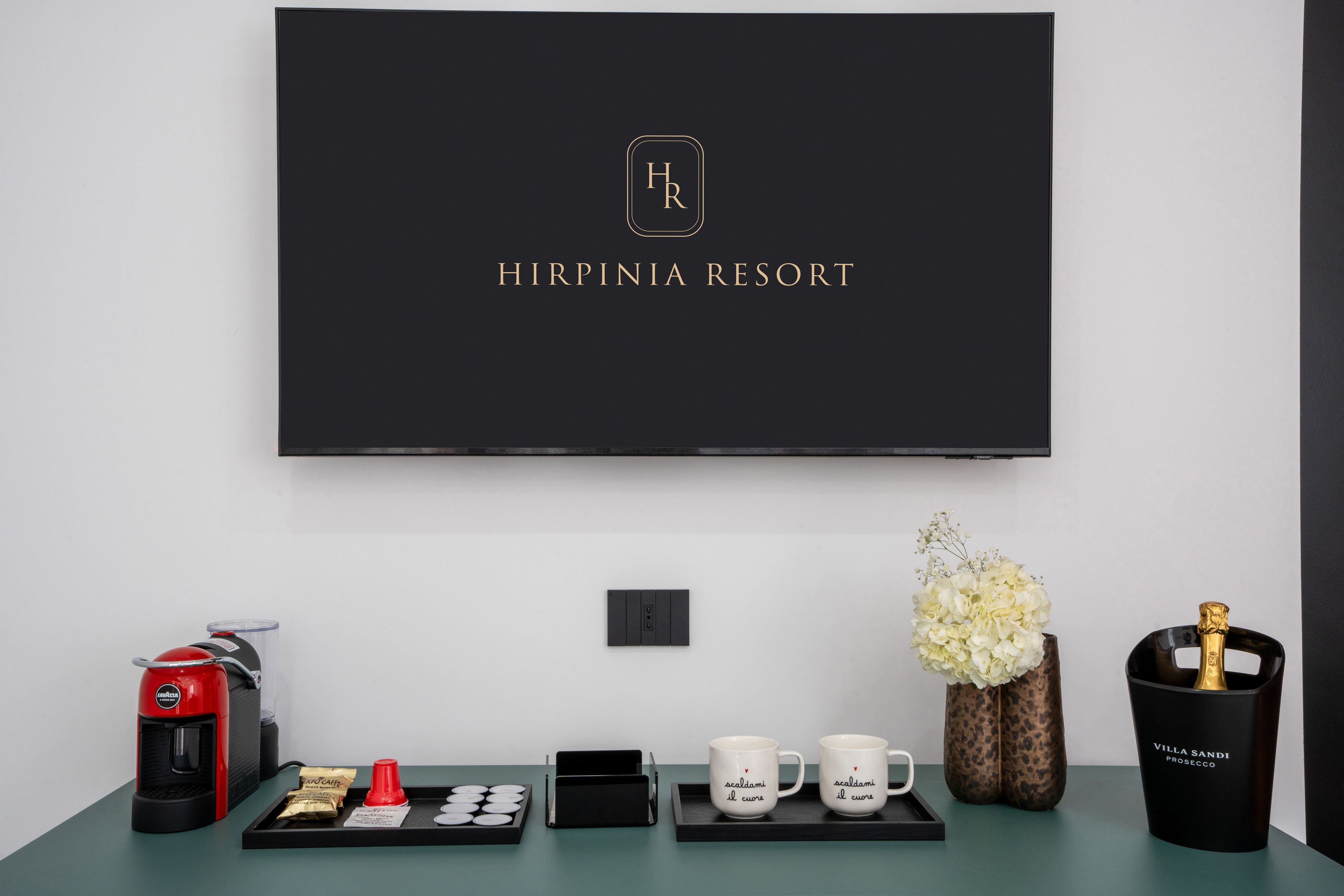 Ein Hotel-Empfangsbereich mit einem schwarzen Schild, auf dem 'HIRPINI RESORT' steht, und einem an der Wand befestigten Flachbildfernseher.