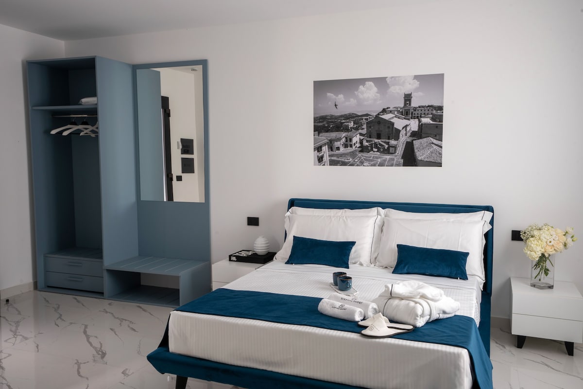 Een keurig opgeruimde slaapkamer met een bed, een kledingkast, een nachtkastje en een aan de muur hangend schilderij.