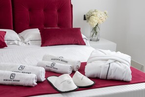 A neatly made bed with red and white bedding, a red headboard, and a vase of white flowers on a bedside table.