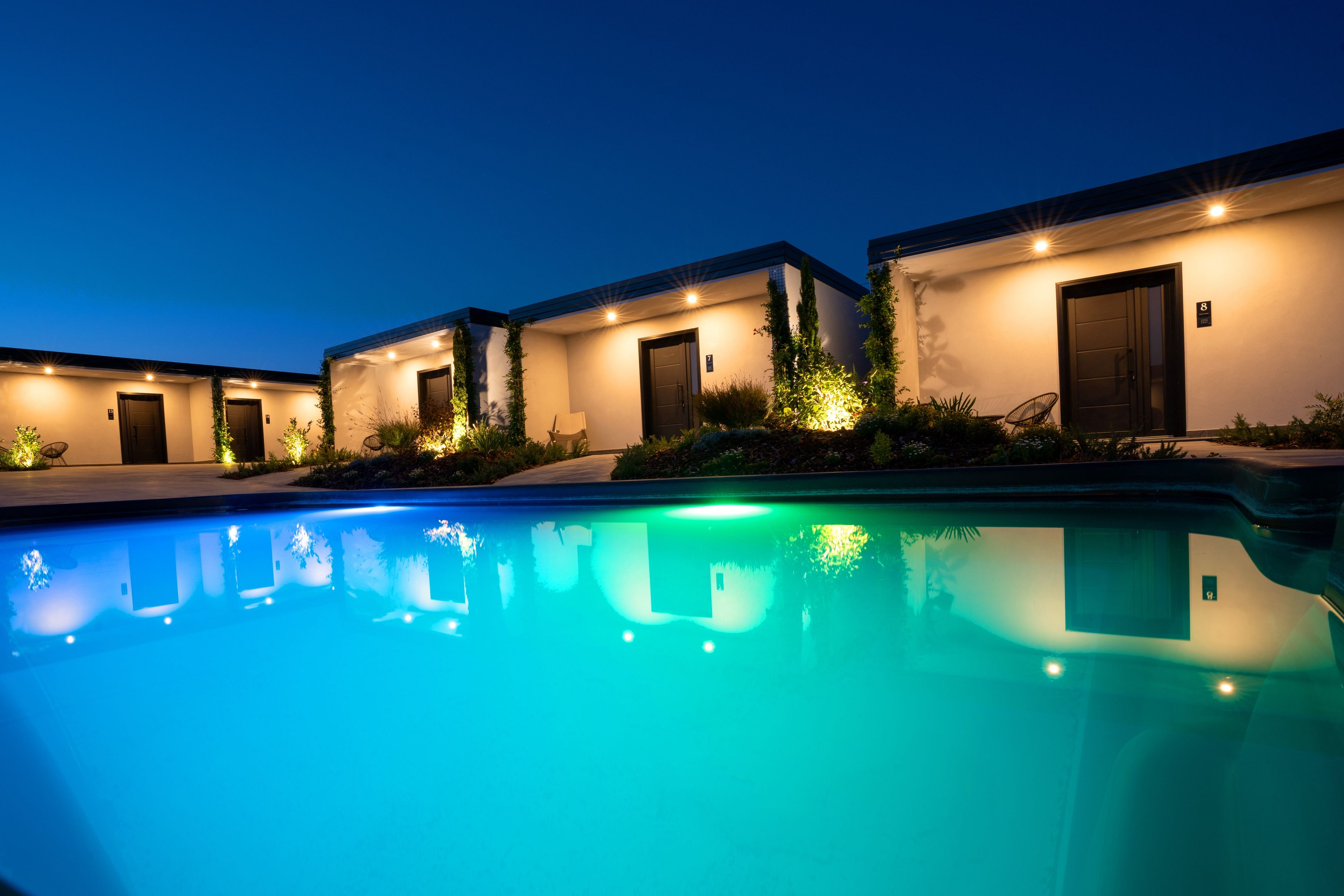 A poolside view of a hotel with multiple buildings, each with a door and a number sign.