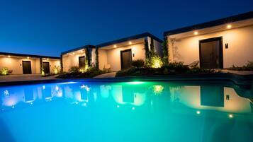 A poolside view of a hotel with multiple buildings, each with a door and a number sign.