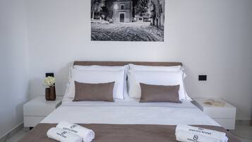 Una camera d'albergo con un letto, due cuscini, un comodino con un telefono, un vaso con fiori e un quadro appeso al muro.