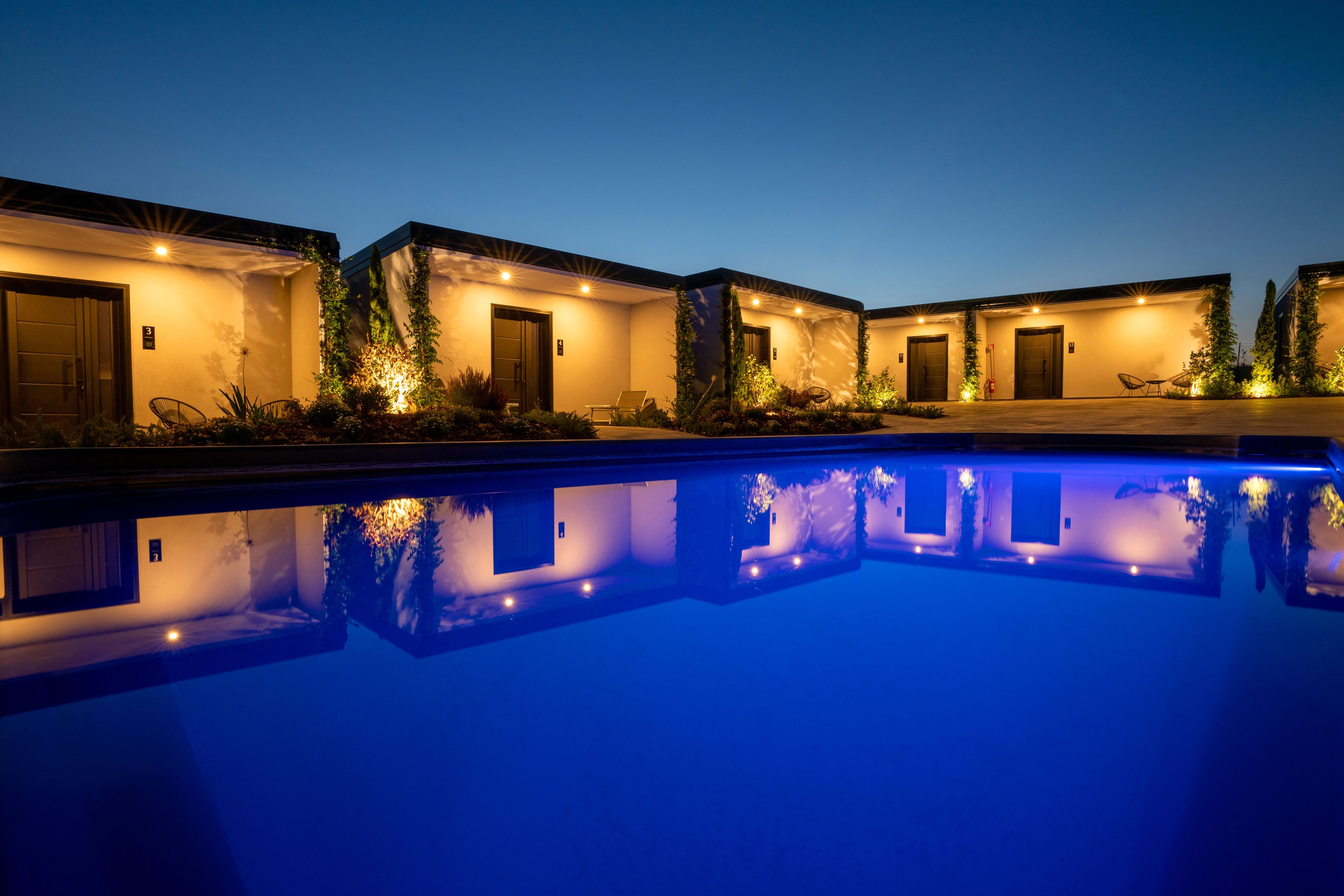 A poolside view of a hotel with multiple rooms, each with a door and a small garden area.