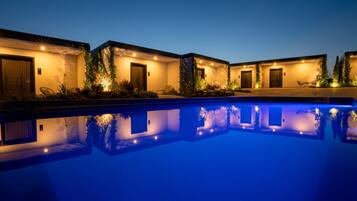 A poolside view of a hotel with multiple rooms, each with a door and a small garden area.