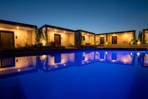 A poolside view of a hotel with multiple rooms, each with a door and a small garden area.