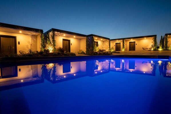 A poolside view of a hotel with multiple rooms, each with a door and a small garden area.