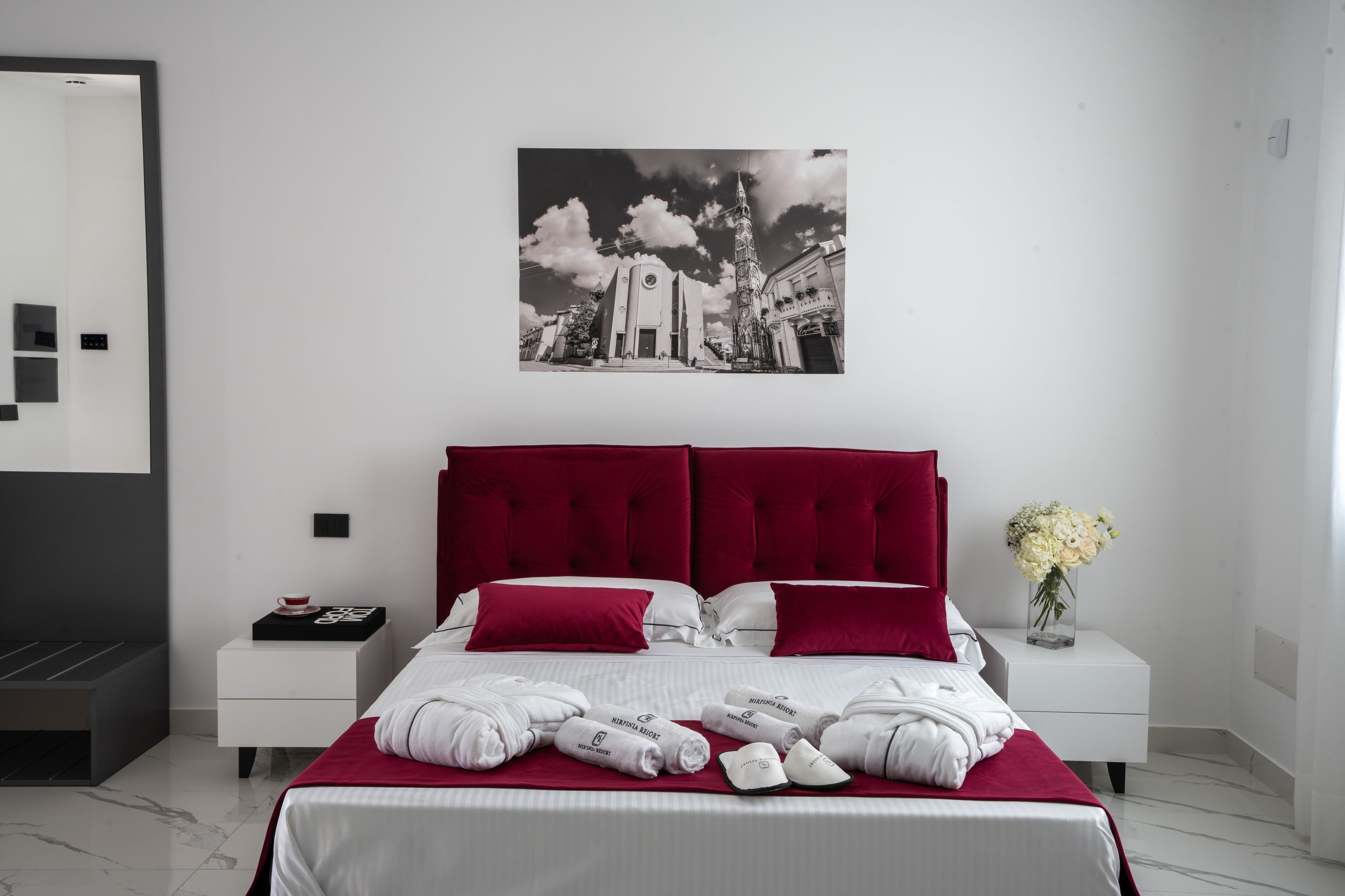 Una habitación de hotel moderna con una cama grande, una mesita de noche, un cuadro en la pared y un florero con flores.