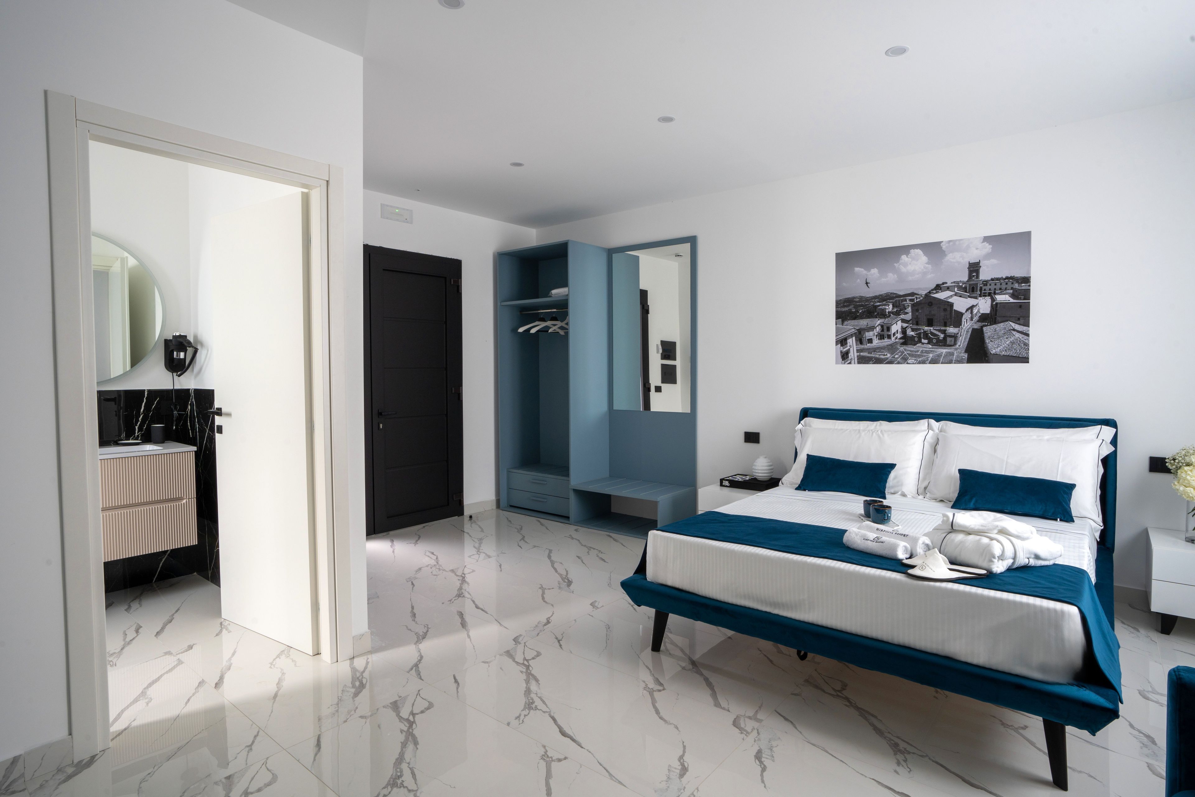 A modern bedroom with a large bed, a walk-in closet, and a bathroom with a marble floor.