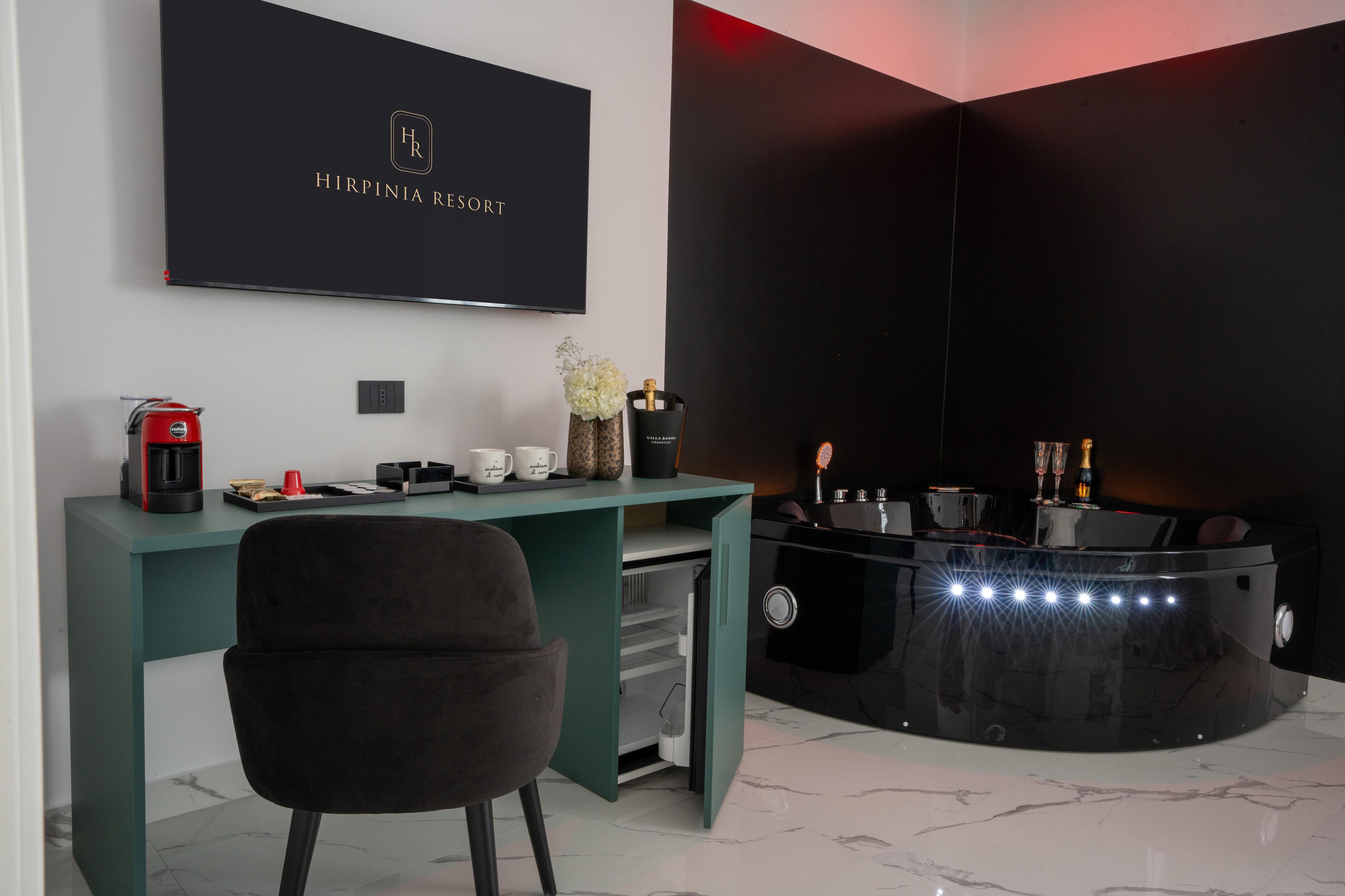 A modern room with a desk, a chair, a flat-screen TV, a minibar, and a decorative vase.